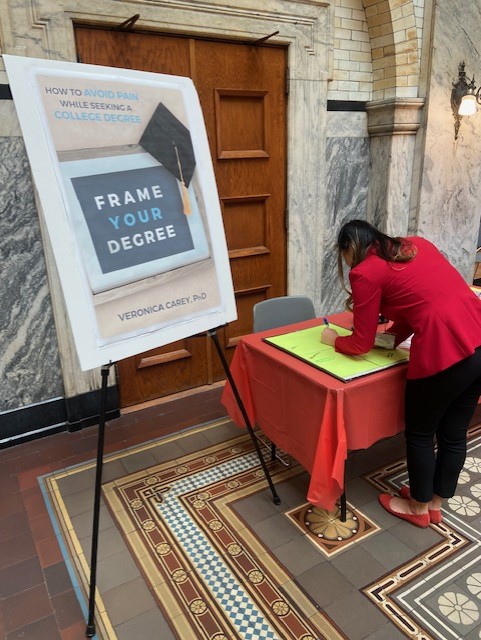 A student in a red top stopping by the Frame Your Degree book table